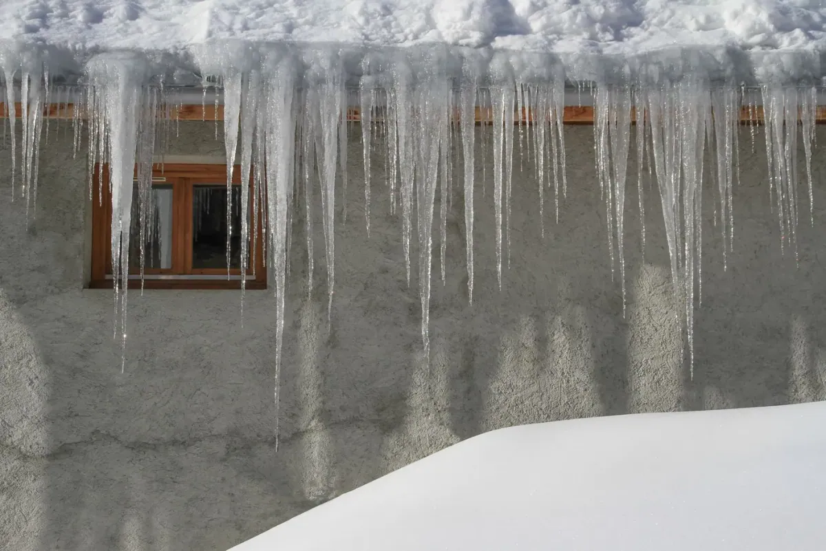 A thick ridge of ice and heavy icicles forming an ice dam along a home's eaves after heavy snow