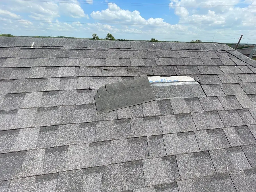 A wind-torn asphalt shingle folded back on an otherwise sound roof, exposing the underlayment beneath